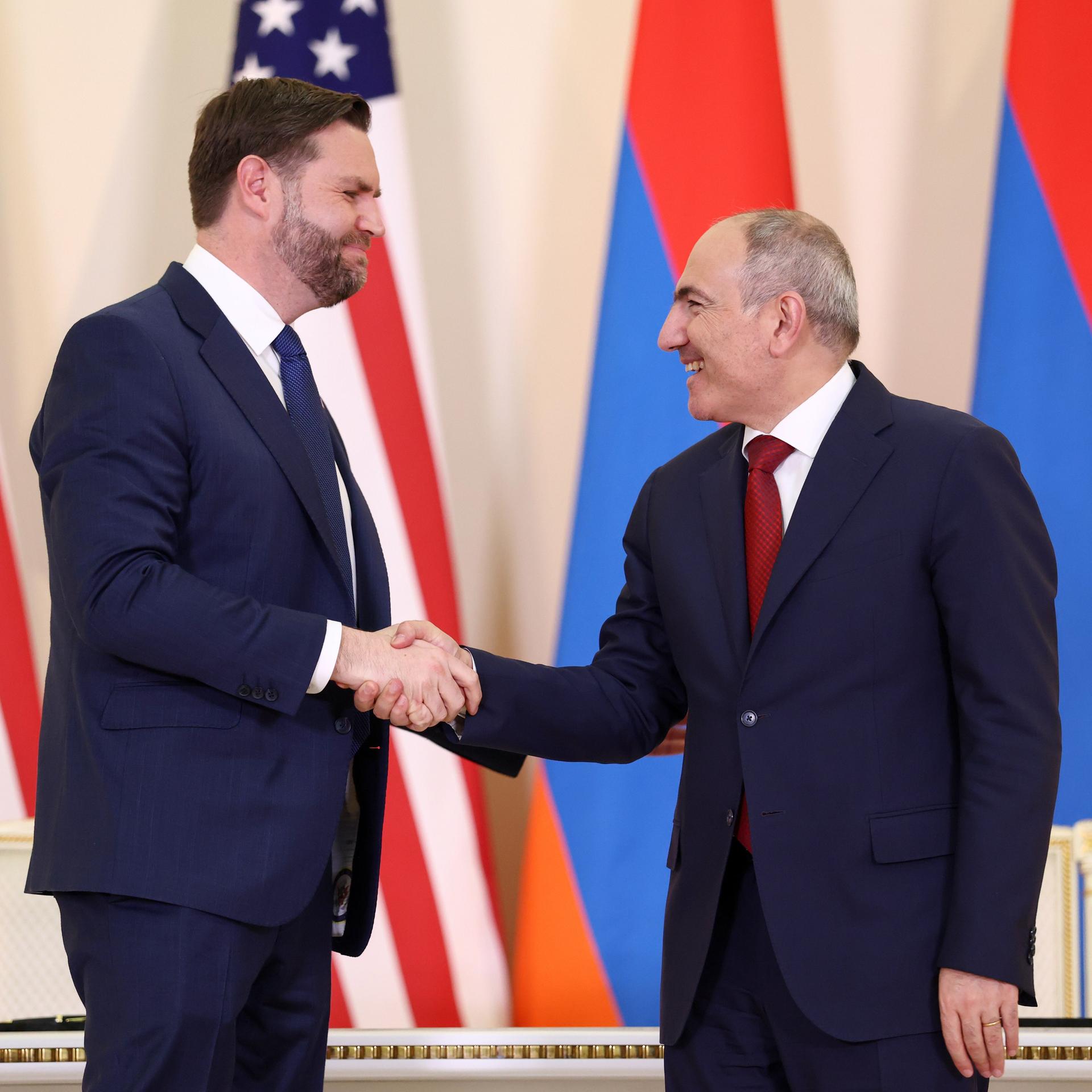 Vance und Paschinjan stehen vor US-Flaggen und armenischen Flaggen und schütteln sich die Hand.