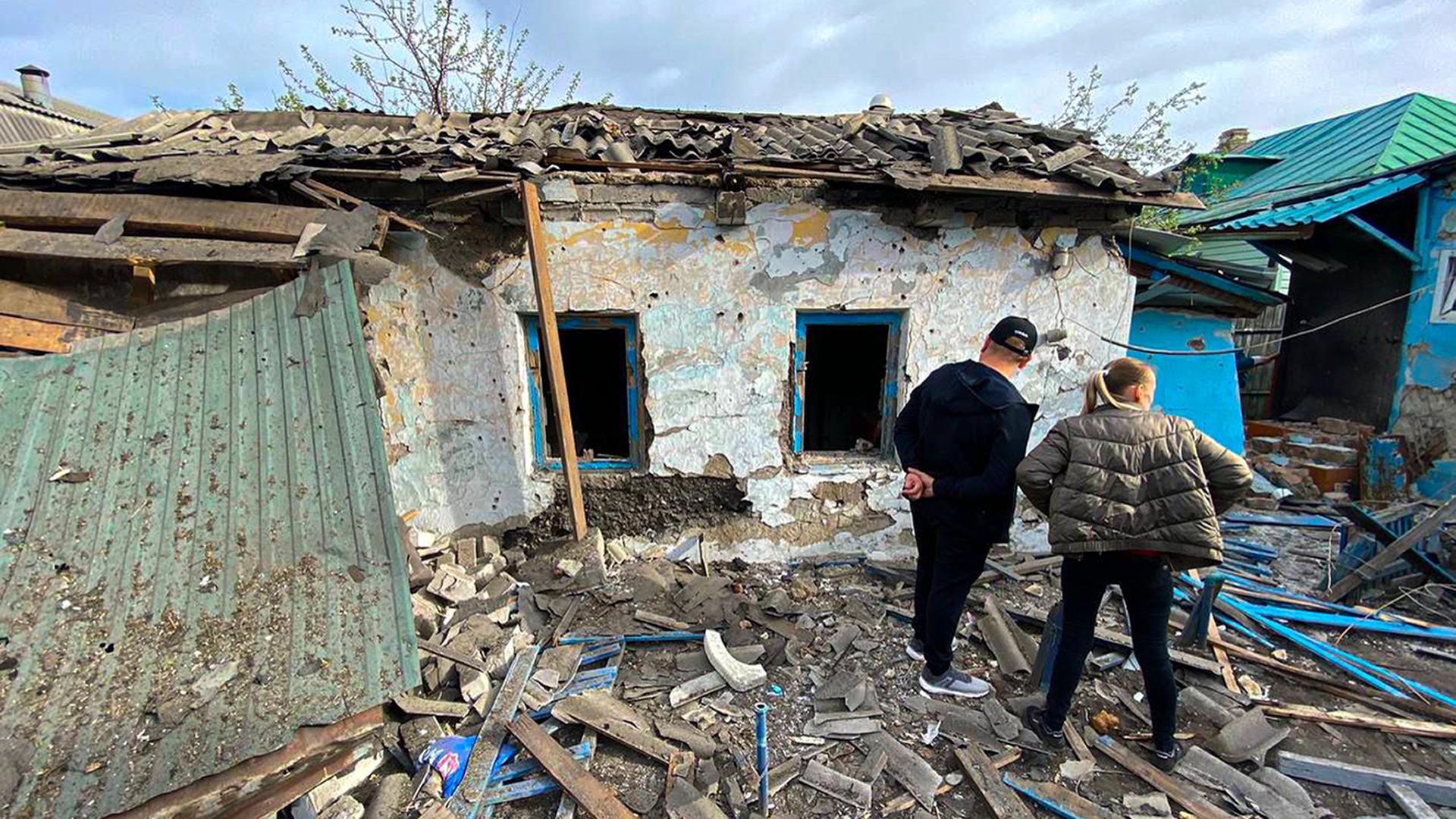 Ein Mann und eine Frau betrachten die Schäden an einem Gebäde in der Region Belgorod. Es liegen Trümmerteile rundherum.