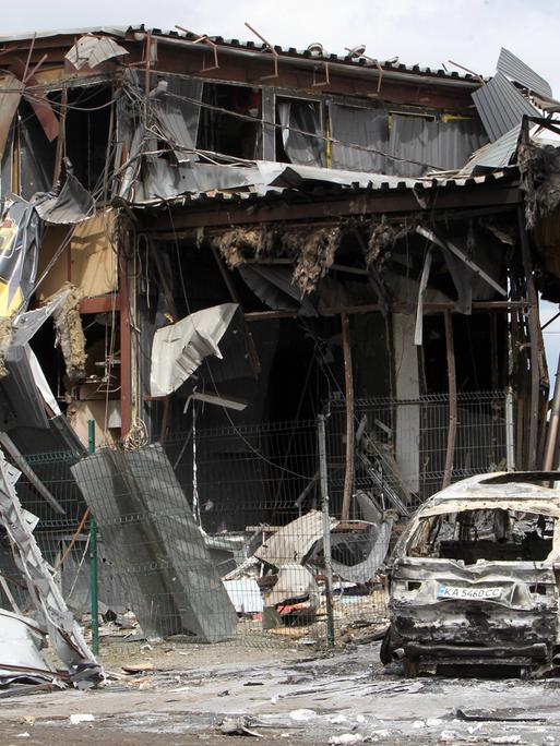 Ein ausgebrannter PKW steht vor einem zerstörten Gebäude. Aufnahme aus der ukrainischen Stadt Dnipro nach einem russischen Raketenangriff.