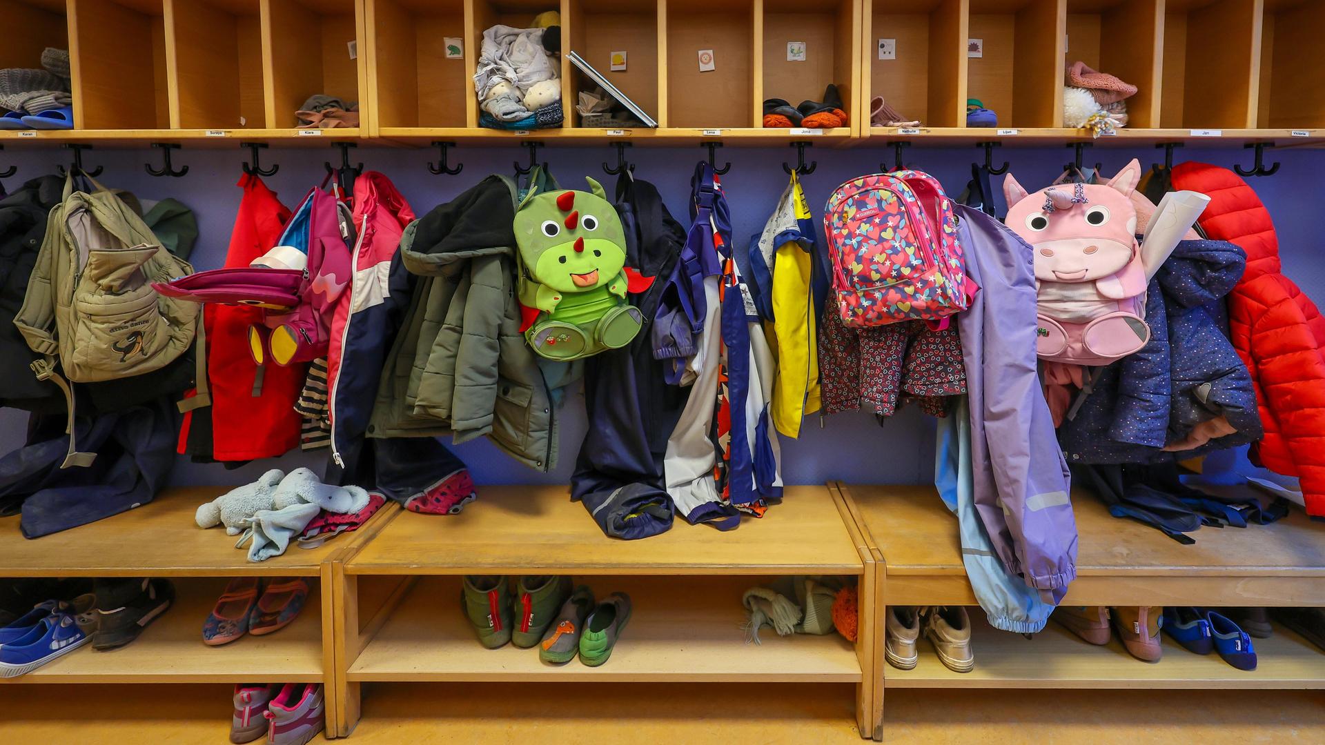Mäntel, Jacken und Rucksäcke von Kindern hängen an einer Garderobe in einer Kita.