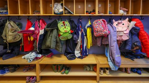 Mäntel, Jacken und Rucksäcke von Kindern hängen an einer Garderobe in einer Kita.