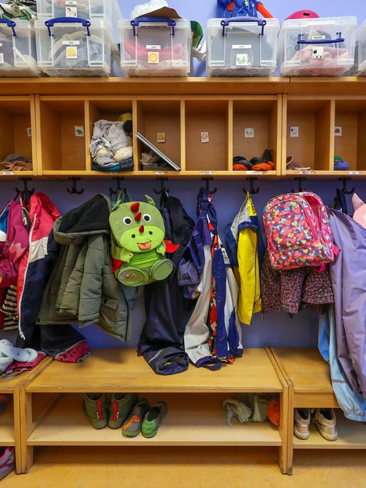 Mäntel, Jacken und Rucksäcke von Kindern hängen an einer Garderobe in einer Kita.
