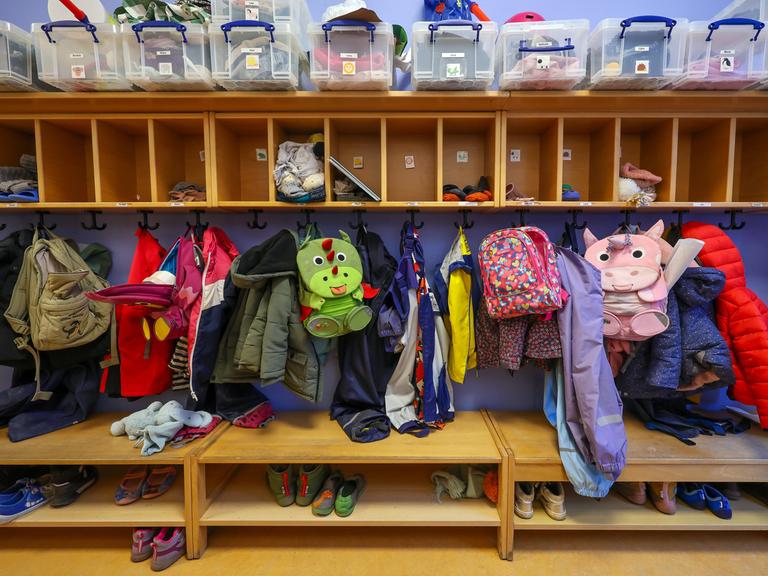 Mäntel, Jacken und Rucksäcke von Kindern hängen an einer Garderobe in einer Kita.