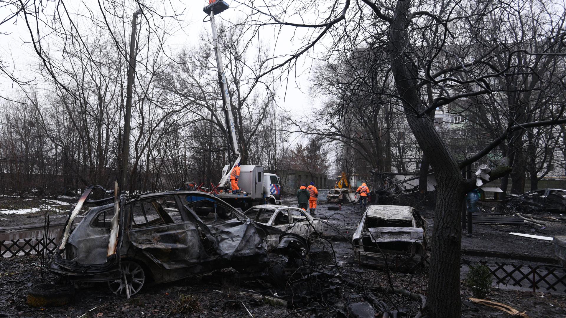 Stadtmitarbeiter reinigen die Stelle in der ukrainischen Stadt Dnipro, an der eine russische Drohne mehrere Autos zerstörte.