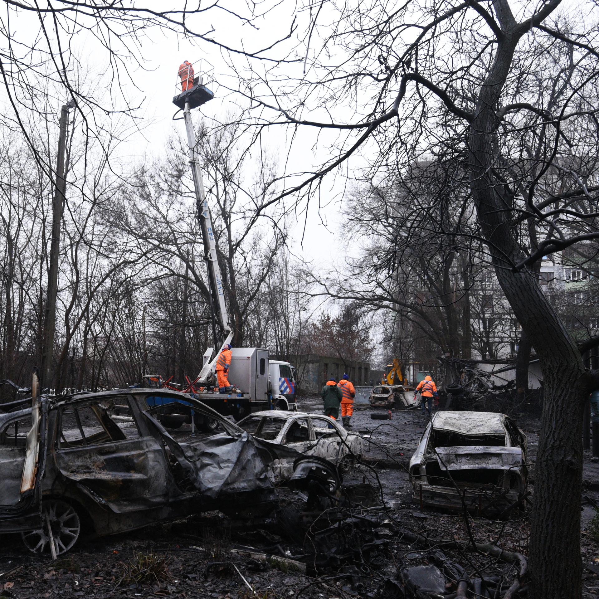 Stadtmitarbeiter reinigen die Stelle in der ukrainischen Stadt Dnipro, an der eine russische Drohne mehrere Autos zerstörte.