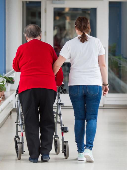 Eine Pflegerin (r) führt eine ältere Frau mit Rollator durch einen Flur im Seniorenzentrum Sankt Elisabeth.
