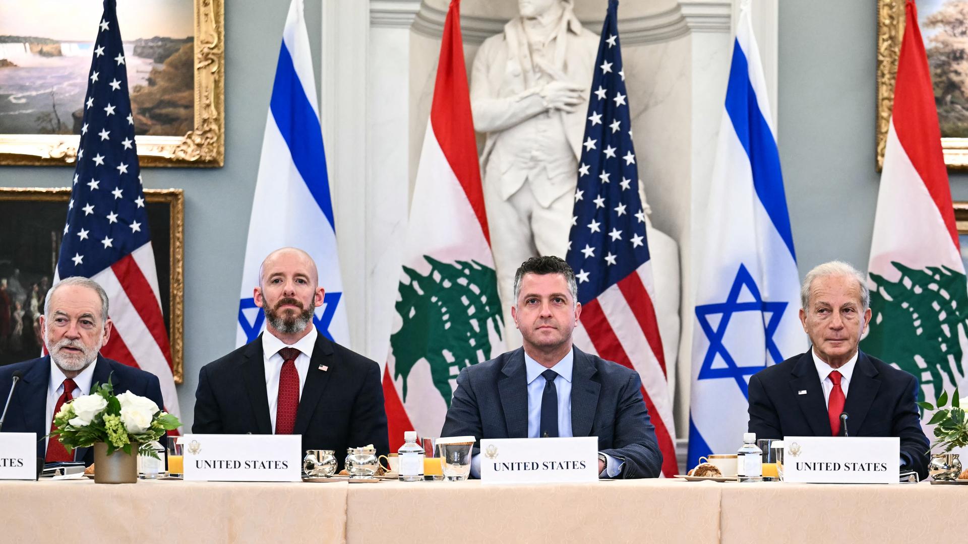 Das Bild zeigt vier Vertreter der US-Vermittlergruppe vor den Flaggen der drei Länder. Sie sitzen nebeneinander an einem Tisch und schauen in die Kamera. 