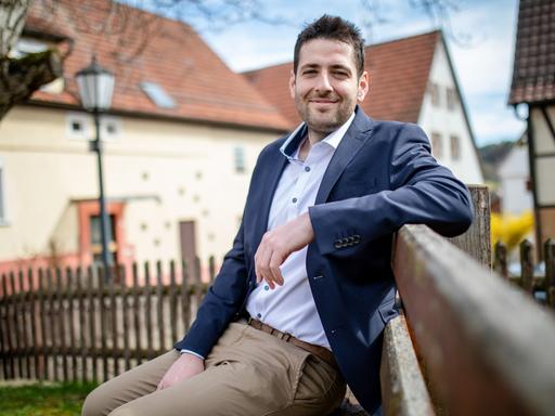 Ryyan Alshebl sitzt auf einer Bank und schaut freundlich in die Kamera.