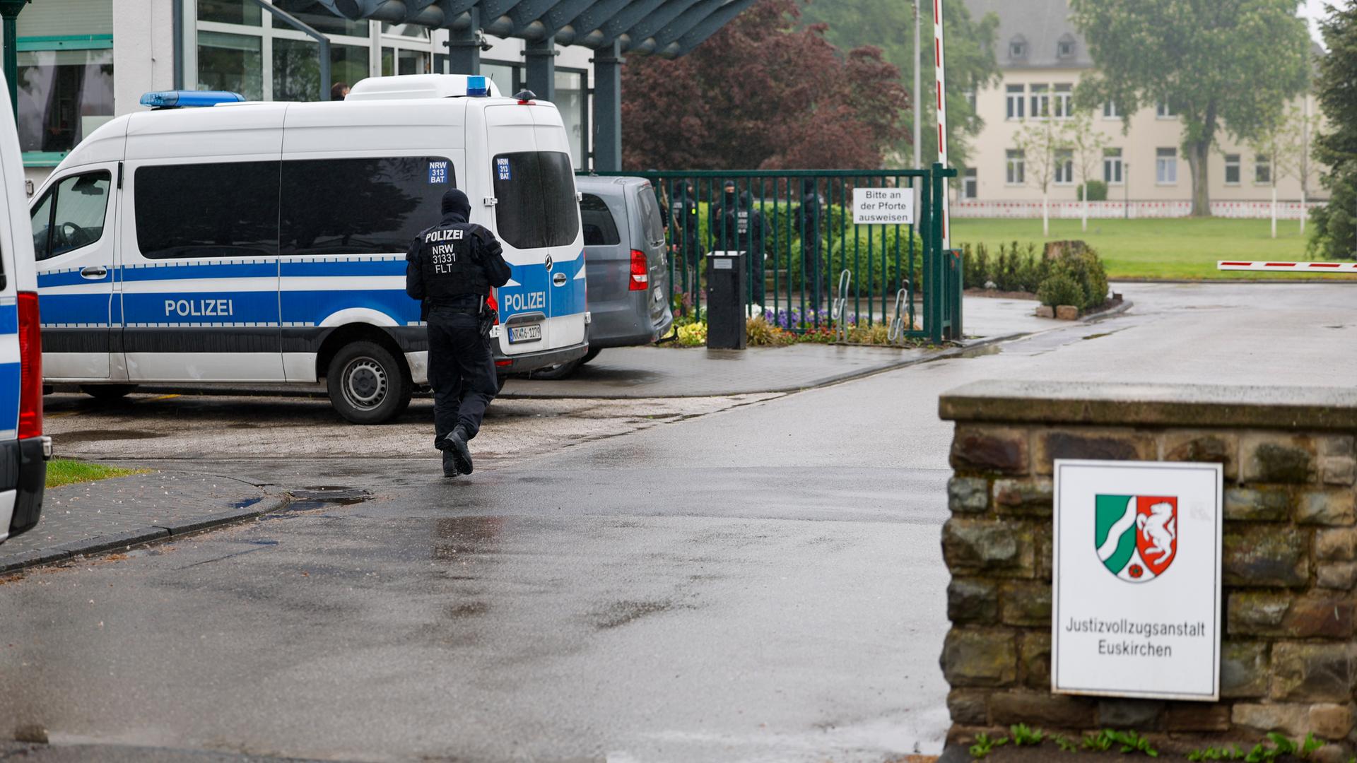 Der Eingang zur Justizvollzugsanstalt Euskirchen. An einer kleinen Mauer hängt ein Schild der JVA. Auf dem Hof steht ein Mannschaftswagen der Polizei, ein Beamter läuft über den Hof. Im Hintergrund sind Gebäude zu sehen.