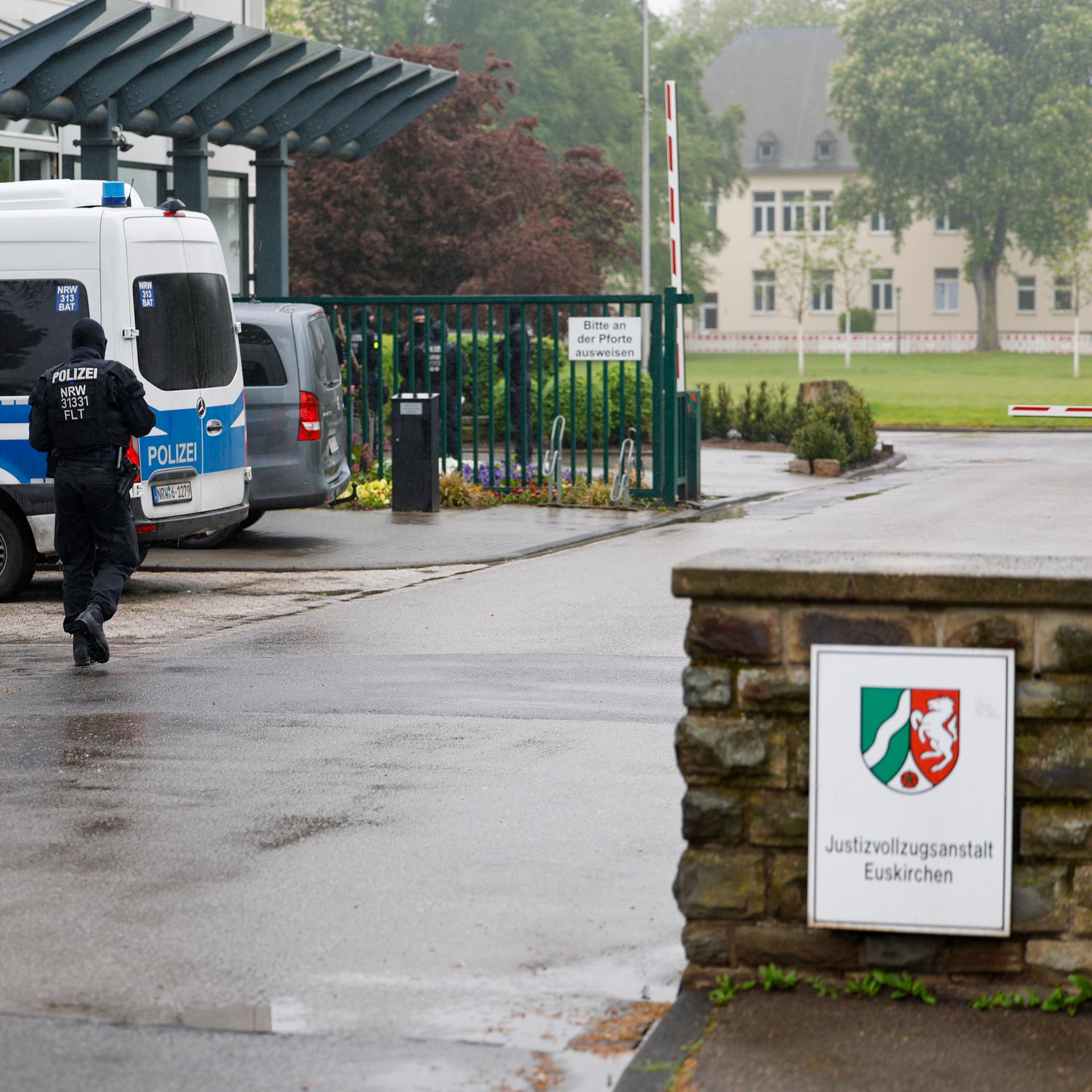 Der Eingang zur Justizvollzugsanstalt Euskirchen. An einer kleinen Mauer hängt ein Schild der JVA. Auf dem Hof steht ein Mannschaftswagen der Polizei, ein Beamter läuft über den Hof. Im Hintergrund sind Gebäude zu sehen.