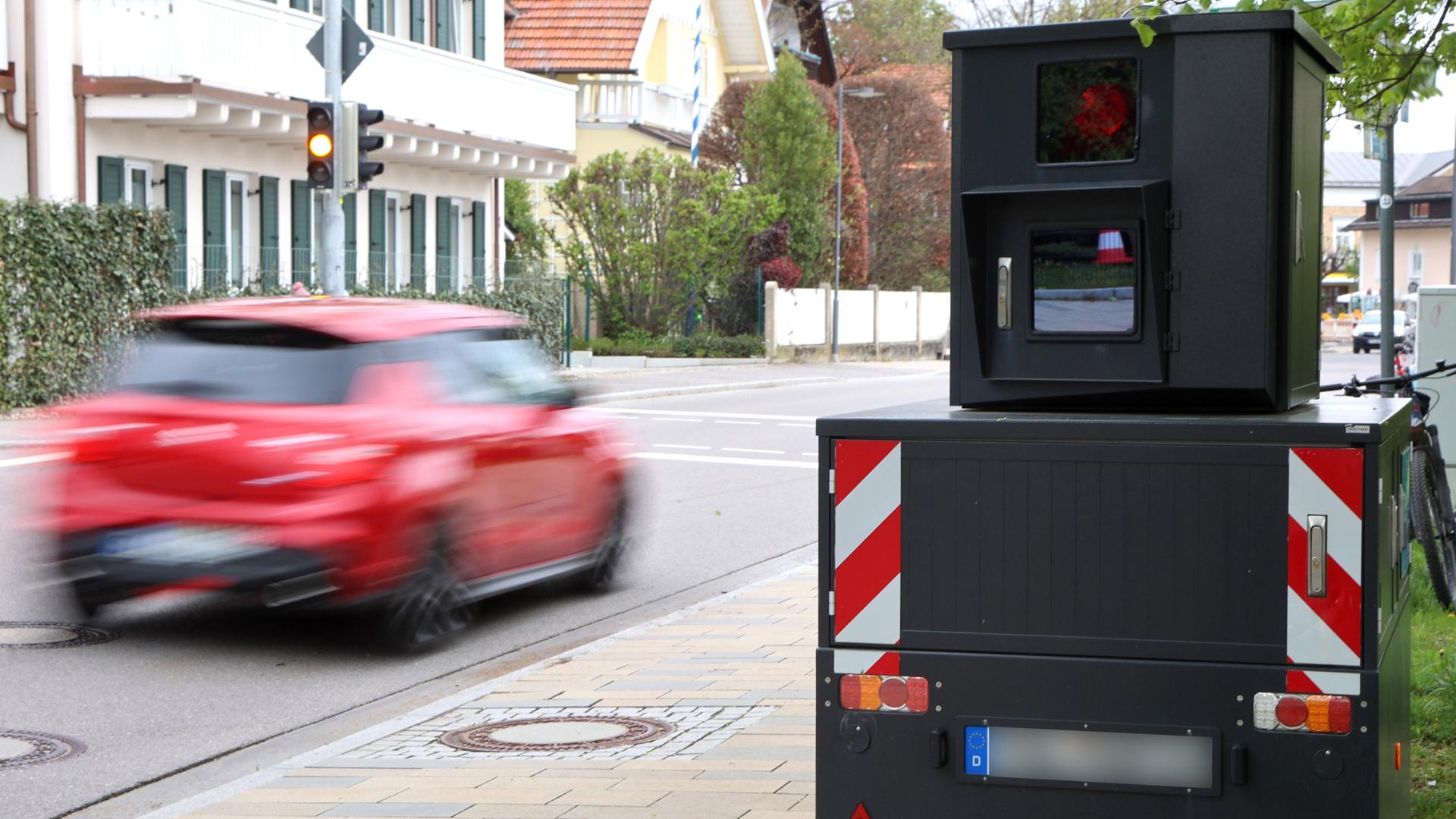 Ein Blitzer steht an einer Ampel in Bayern, während ein Auto vorbeirauscht.