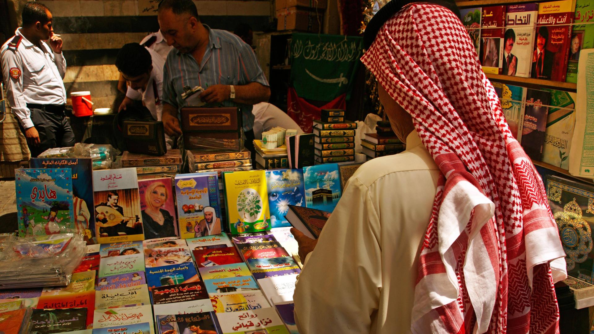  Ein Mann mit Kufiya von hinten. Er steht vor einem Stand mit vielen Büchern. 