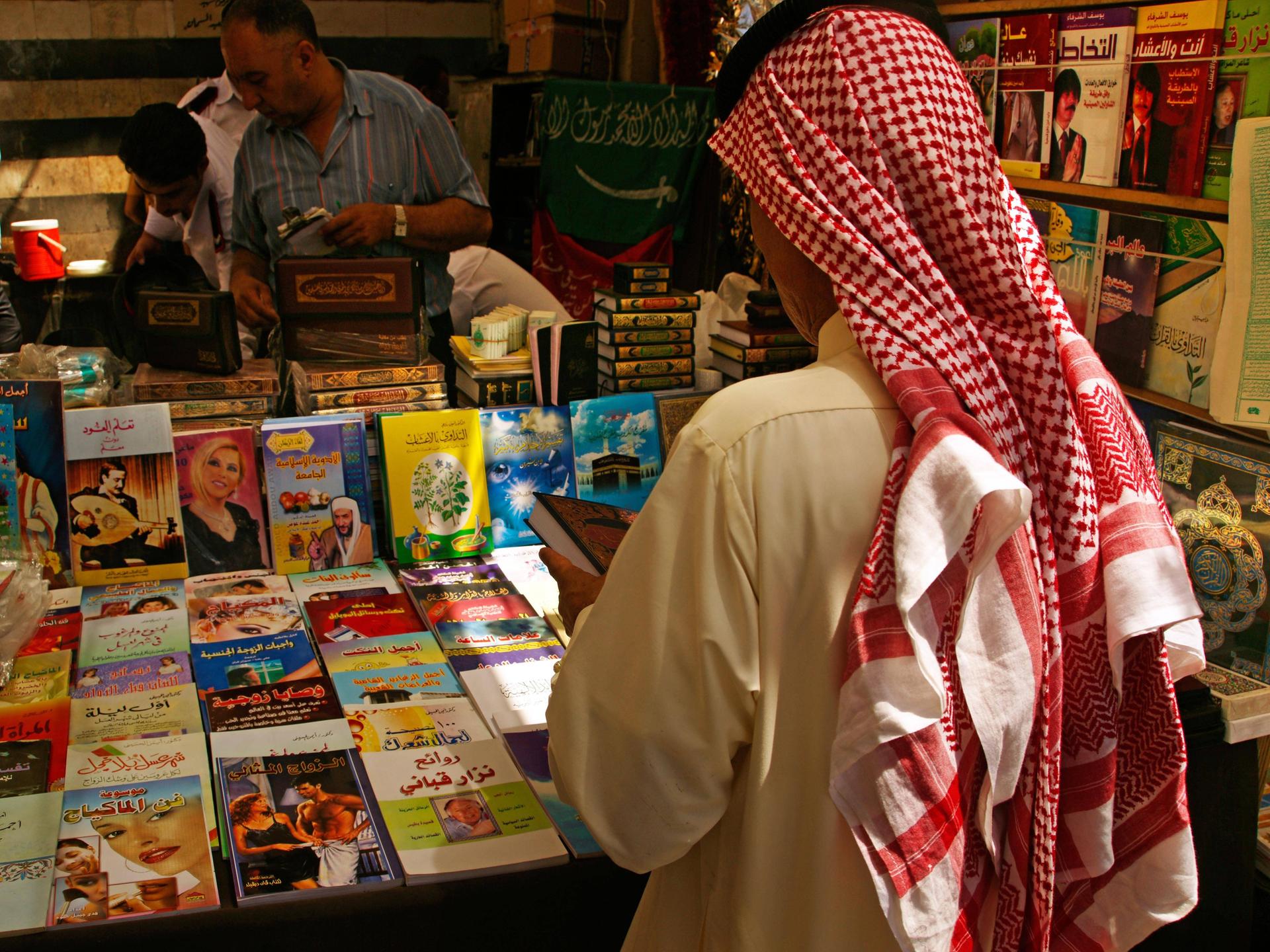  Ein Mann mit Kufiya von hinten. Er steht vor einem Stand mit vielen Büchern. 