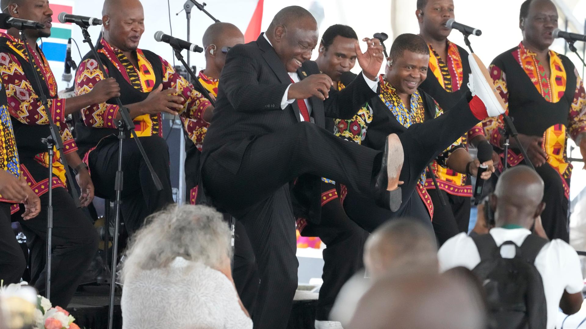 Ramaphosa bewegt sich tanzend auf einer Bühne, hinter ihm spielt eine Band.