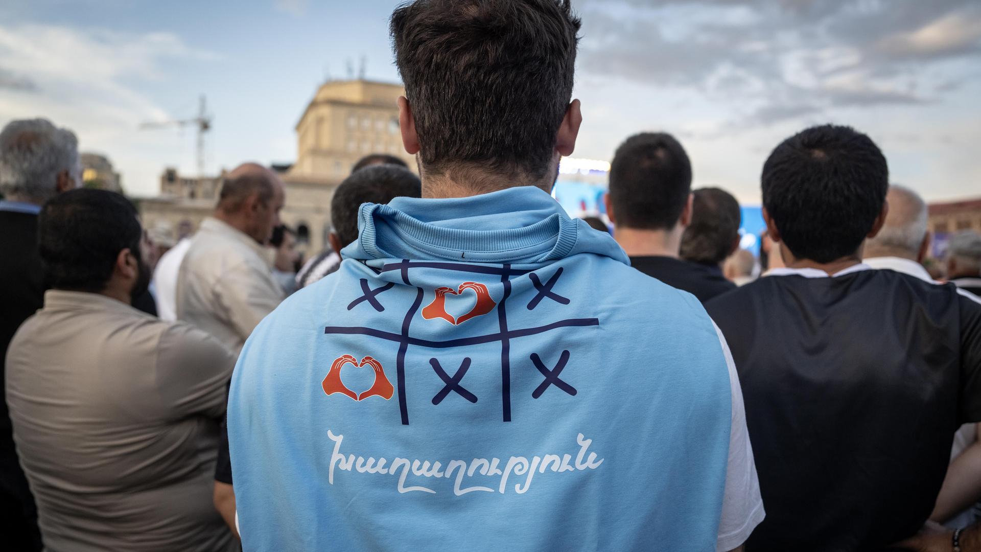 Rückansicht von Anhängern des armenischen Premierministers Nikol Paschinjan. Sie hören ihrem Favoriten bei einer Wahlkampfveranstaltung unter freiem Himmel konzentriert zu.