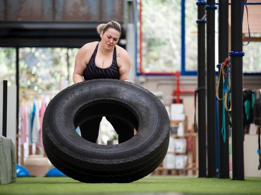 Eine Frau macht Krafttraining, in dem sie einen großen schweren Autoreifen bewegt.