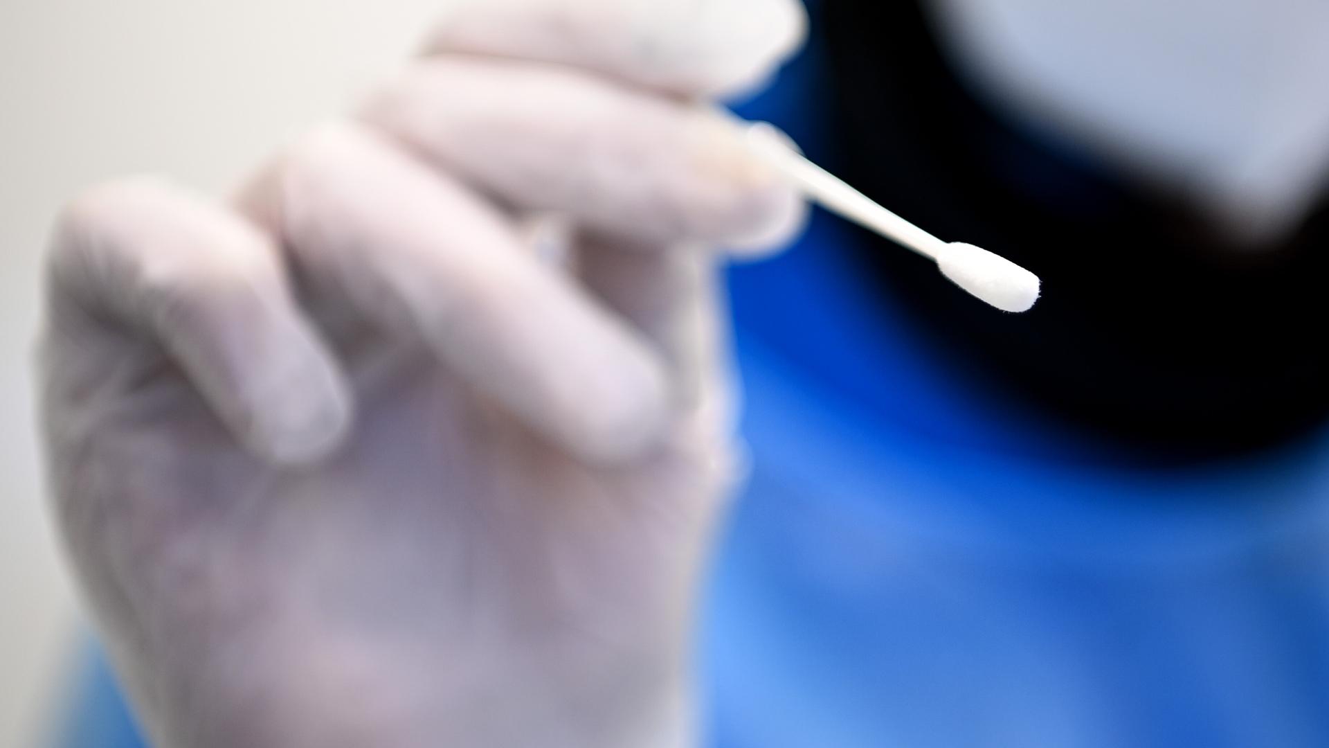 Ein Arzt hält ein Teststäbchen für die Entnahme einer Probe für einen PCR-Test in der Hand.