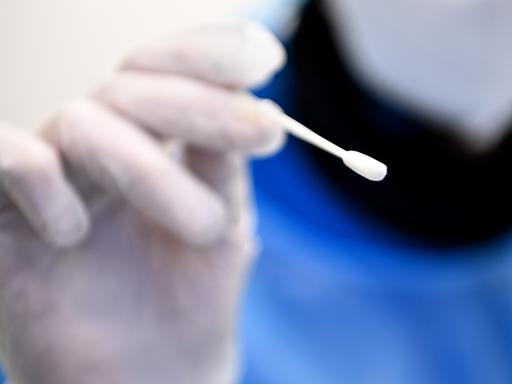 Ein Arzt hält ein Teststäbchen für die Entnahme einer Probe für einen PCR-Test in der Hand.
