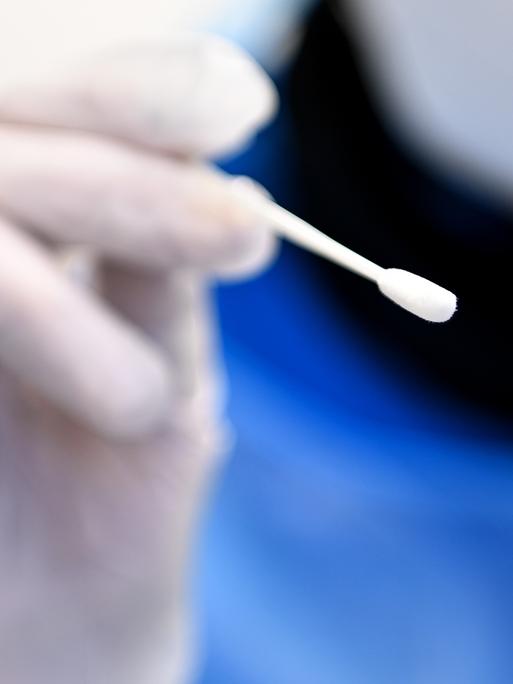 Ein Arzt hält ein Teststäbchen für die Entnahme einer Probe für einen PCR-Test in der Hand.