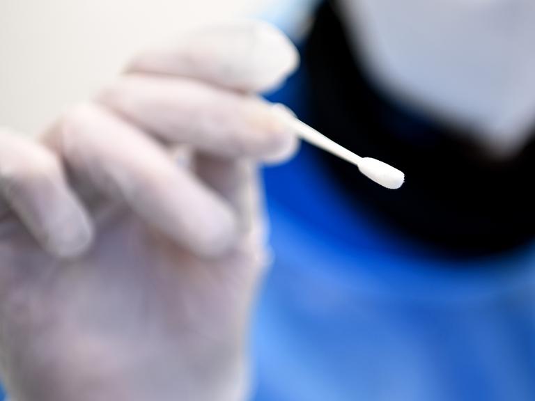 Ein Arzt hält ein Teststäbchen für die Entnahme einer Probe für einen PCR-Test in der Hand.
