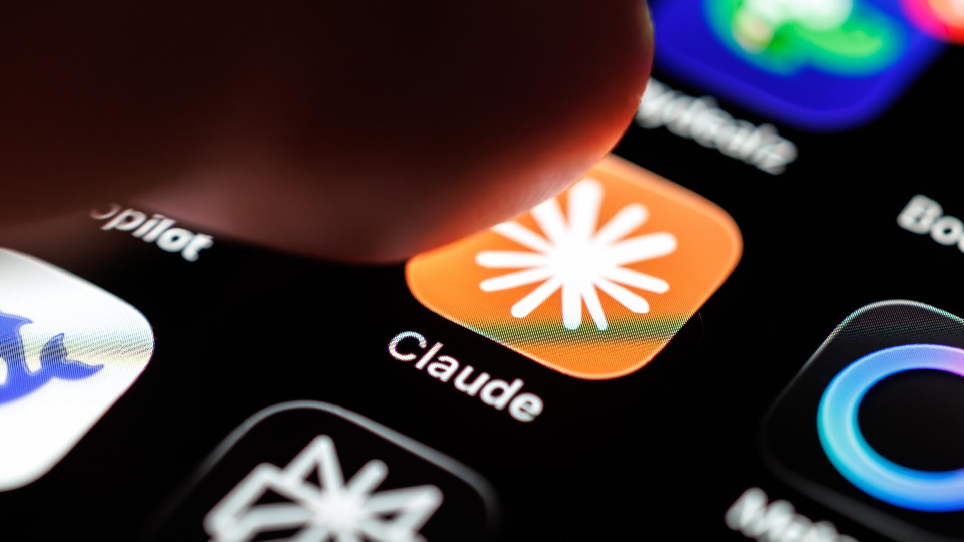 Das Logo der App Claude ist auf dem Display eines Smartphones zu sehen, während ein Finger auf das Symbol tippt. Das Logo der App Claude ist auf dem Display eines Smartphones zu sehen, während ein Finger auf das Symbol tippt.