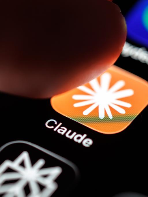Das Logo der App Claude ist auf dem Display eines Smartphones zu sehen, während ein Finger auf das Symbol tippt.