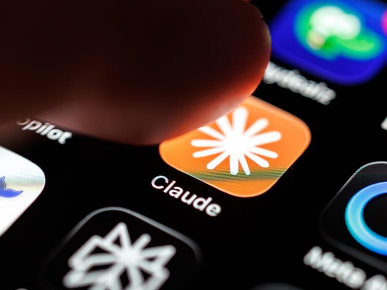 Das Logo der App Claude ist auf dem Display eines Smartphones zu sehen, während ein Finger auf das Symbol tippt.