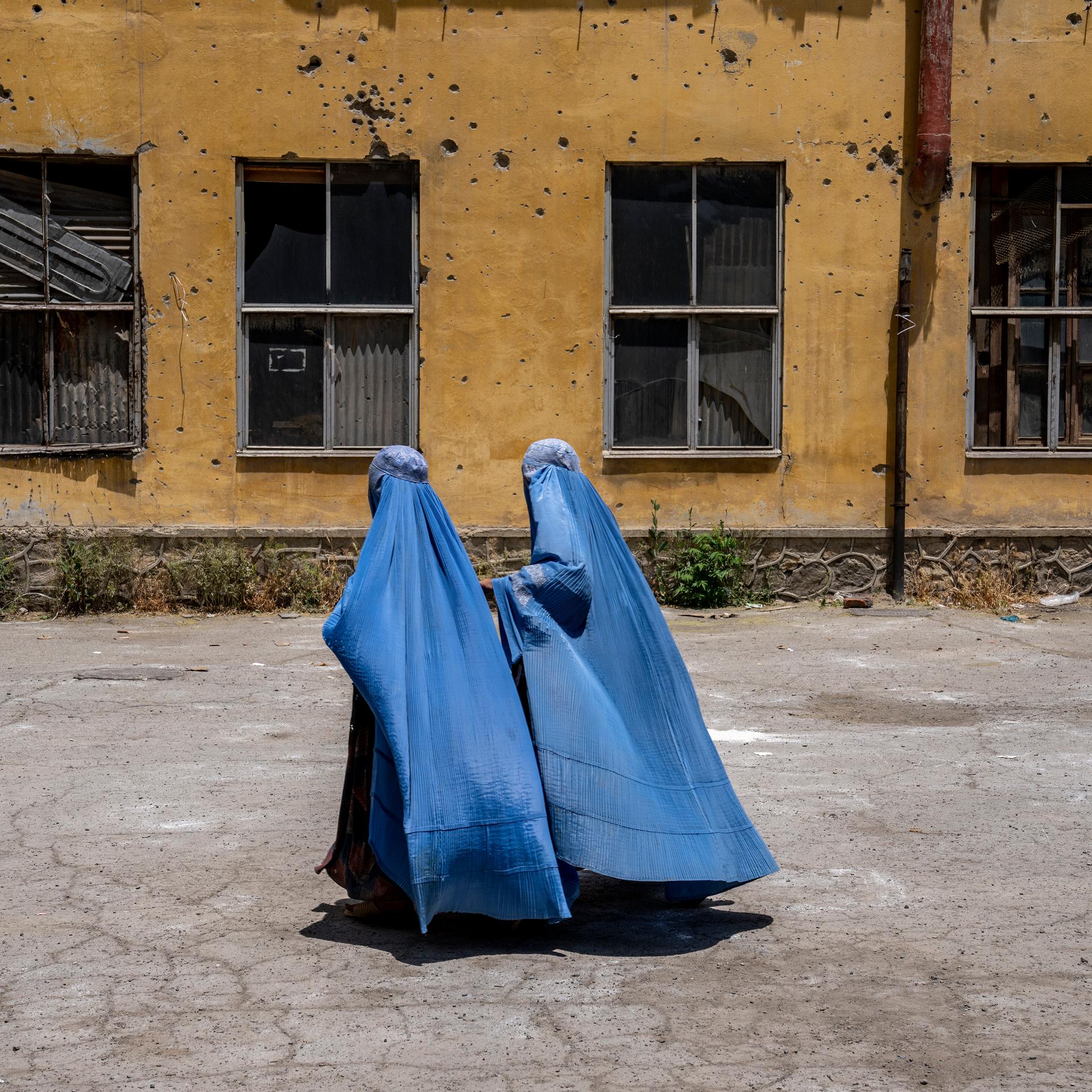 Afghanische Frauen in Burkas gehen an einer zerstörten Hauswand in Kabul vorbei.