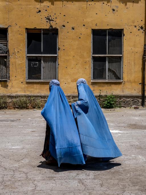 Afghanische Frauen in Burkas gehen an einer zerstörten Hauswand in Kabul vorbei.