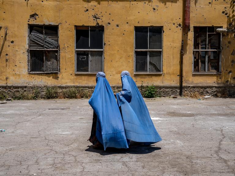 Afghanische Frauen in Burkas gehen an einer zerstörten Hauswand in Kabul vorbei.