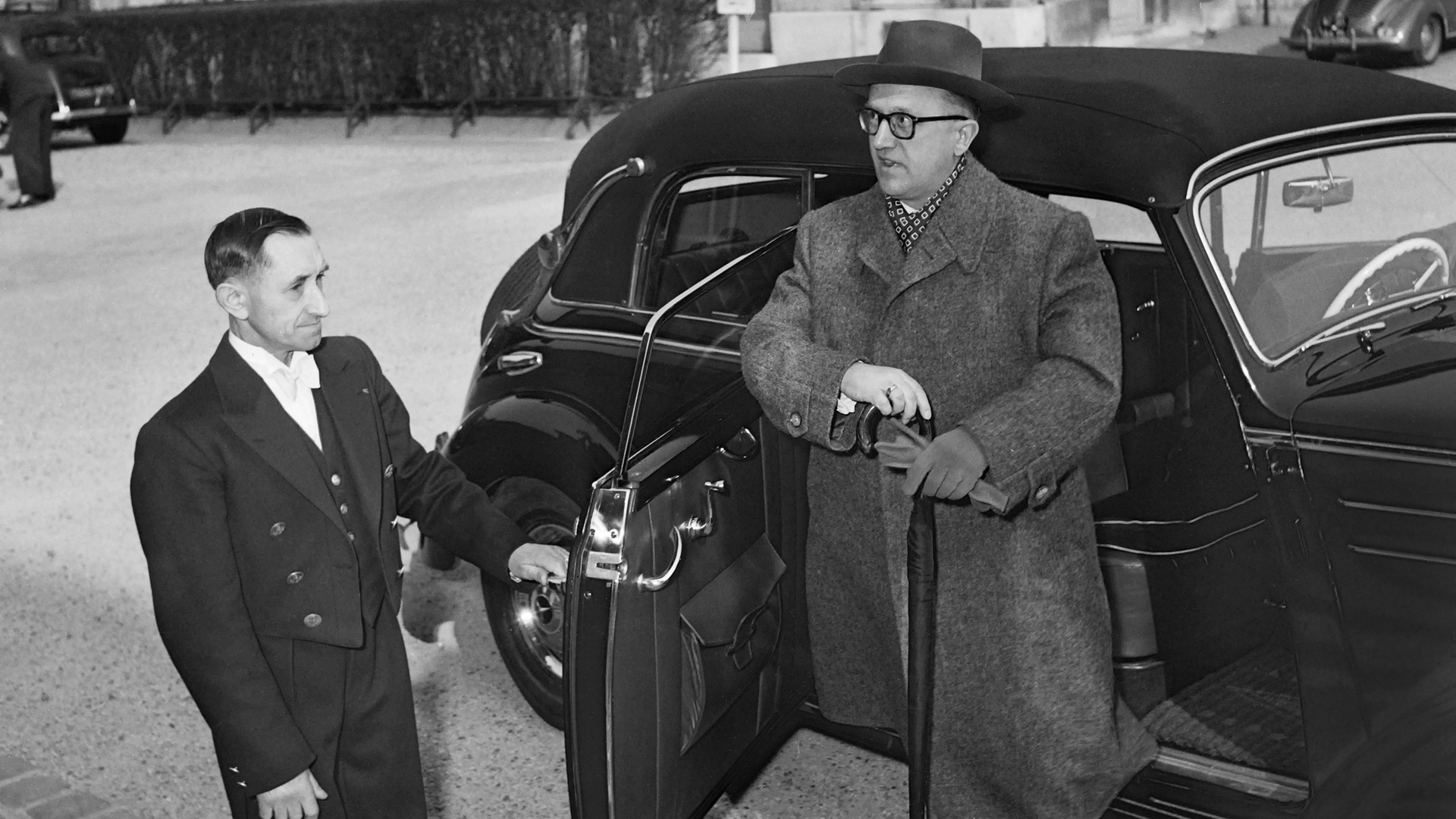Staatssekretär Walter Hallstein steigt aus einem Auto aus. Ein livrierter Page öffnet die Tür. Diese öffnet entgegen der eigentlichen Fahrtrichtung des Gefährts.