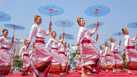 Frauen in identischen traditionellen Kostümen und mit Schirmen in den Händen tanzen während einer Parade synchron. Frauen in identischen traditionellen Kostümen und mit Schirmen in den Händen tanzen während einer Parade synchron.