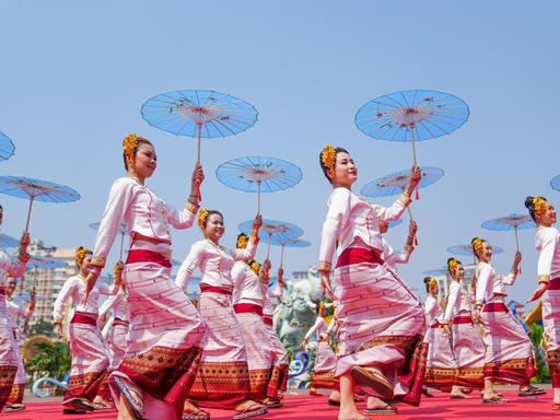 Frauen in identischen traditionellen Kostümen und mit Schirmen in den Händen tanzen während einer Parade synchron.