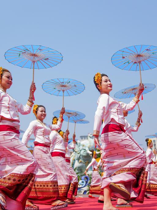 Frauen in identischen traditionellen Kostümen und mit Schirmen in den Händen tanzen während einer Parade synchron.