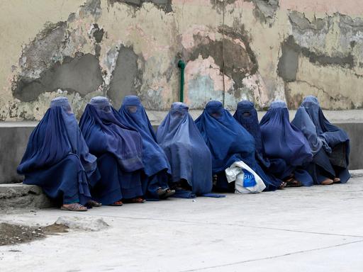 Mehrere afghanischen Frauen sitzen komplett verschleiert durch Burkas auf Rinnstein an der Straße. 