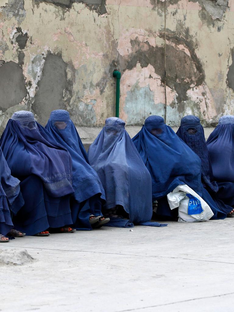 Mehrere afghanischen Frauen sitzen komplett verschleiert durch Burkas auf Rinnstein an der Straße. 