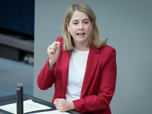 Verena Hubertz, in einem roten Sakko, spricht am Rednerpult des Deutschen Bundestags.