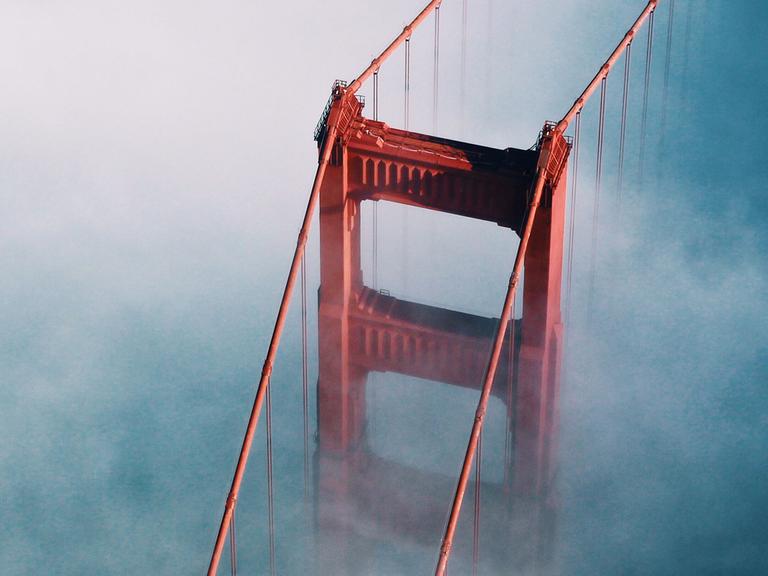 Unterwegs nach San Francisco muss van Dusen einen kühlen Kopf bewahren. Zu sehen: Ein Pfeiler der Golden Gate Bridge von oben in Wolken gehüllt. 