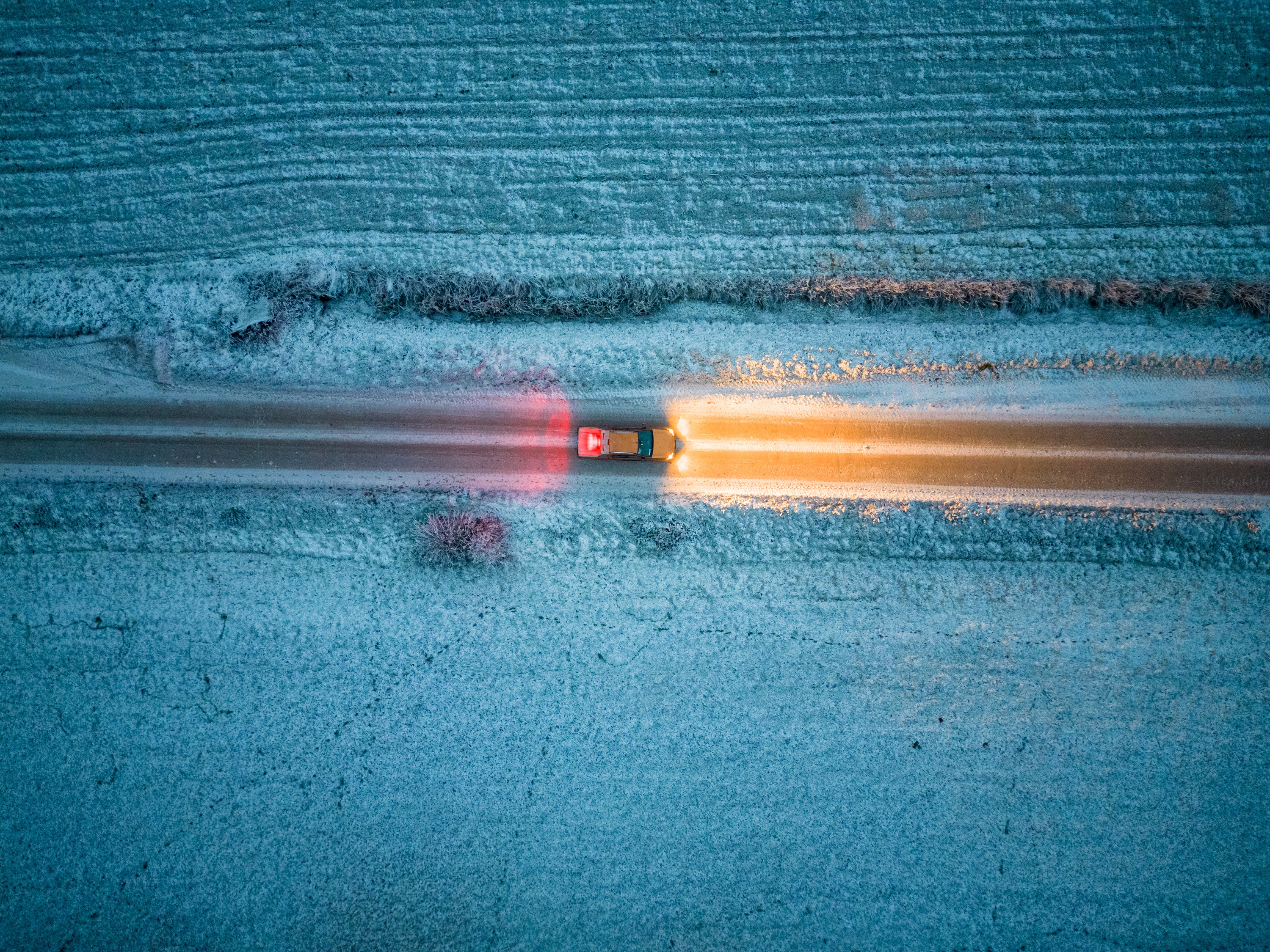 Vogelperspektive auf ein Auto, das im Dunkeln durch eine Schneelandschaft fährt.