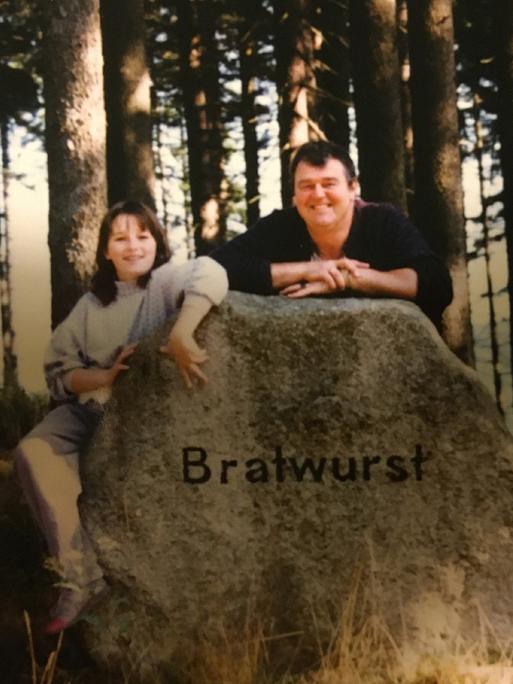 Eine Frau und ein Mann stehen hinter einem großen Stein, auf dem "Bratwurst" steht.