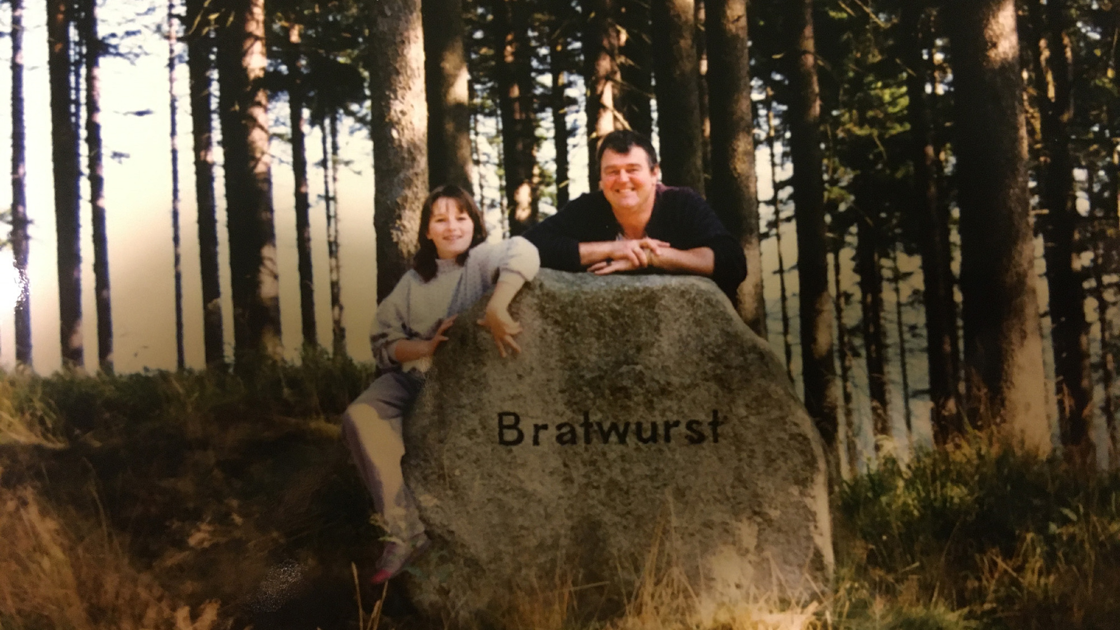 Eine Frau und ein Mann stehen hinter einem großen Stein, auf dem "Bratwurst" steht.