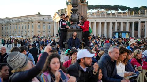 Das Bild zeigt zahlreiche Menschen, die am frühen Morgen zum Petersplatz gekommen sind, um an den Beerdigungsfeierlichkeiten für Papst Franziskus teilzunehmen. 