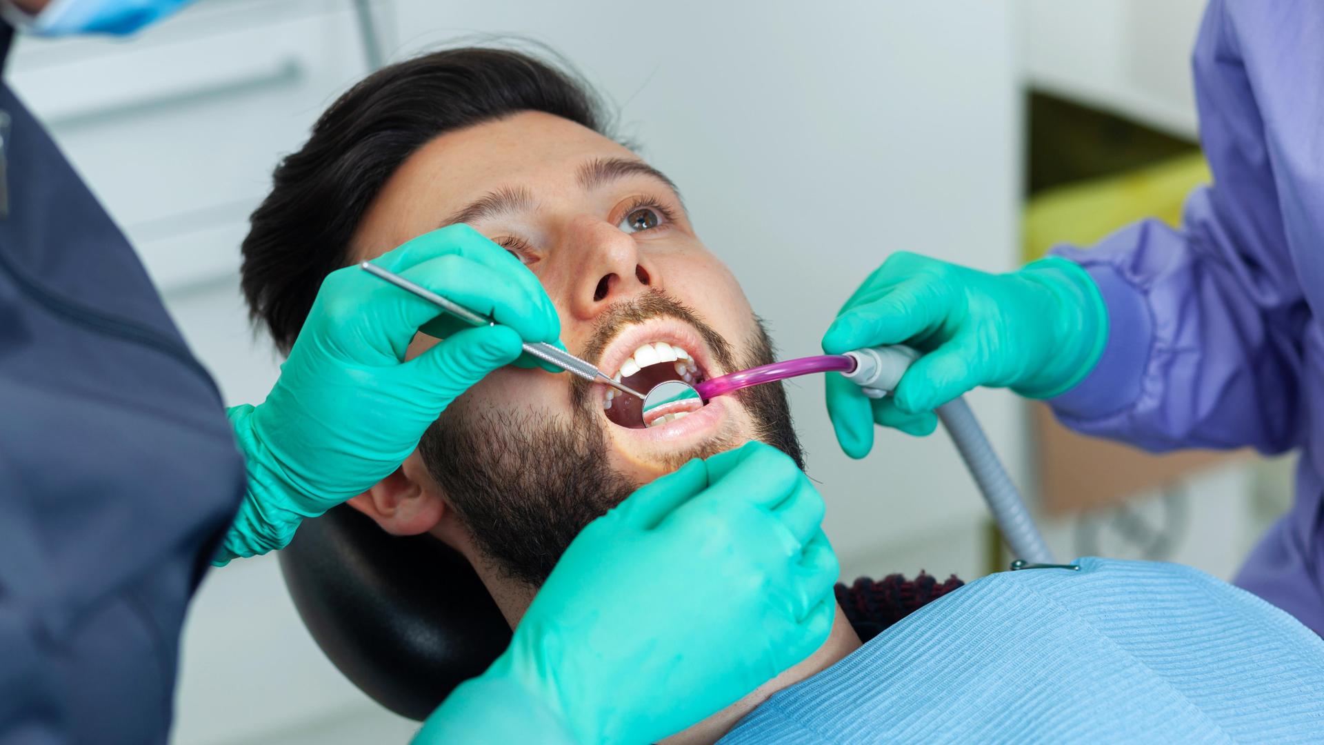 Eine Zahnärztin untersucht einen männlichen Patienten in einer Zahnarztpraxis mit professionellem Werkzeug und persönlicher Schutzausrüstung.