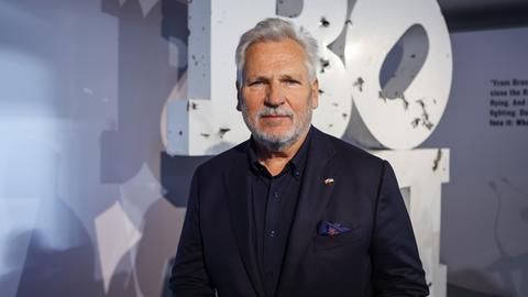 Polens früherer Staatschef Aleksander Kwaśniewski steht in einem dunklen Anzug vor einer Wand auf der große Buchstaben zu sehen sind
