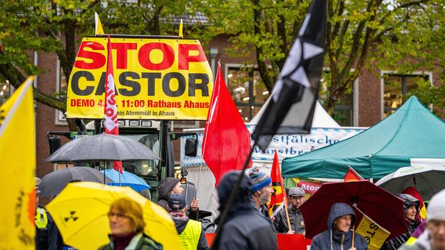 Zu sehen ist ein Banner mit der Aufschrift "Stop Castor". Daneben stehen Menschen mit Regen-Schirmen.
