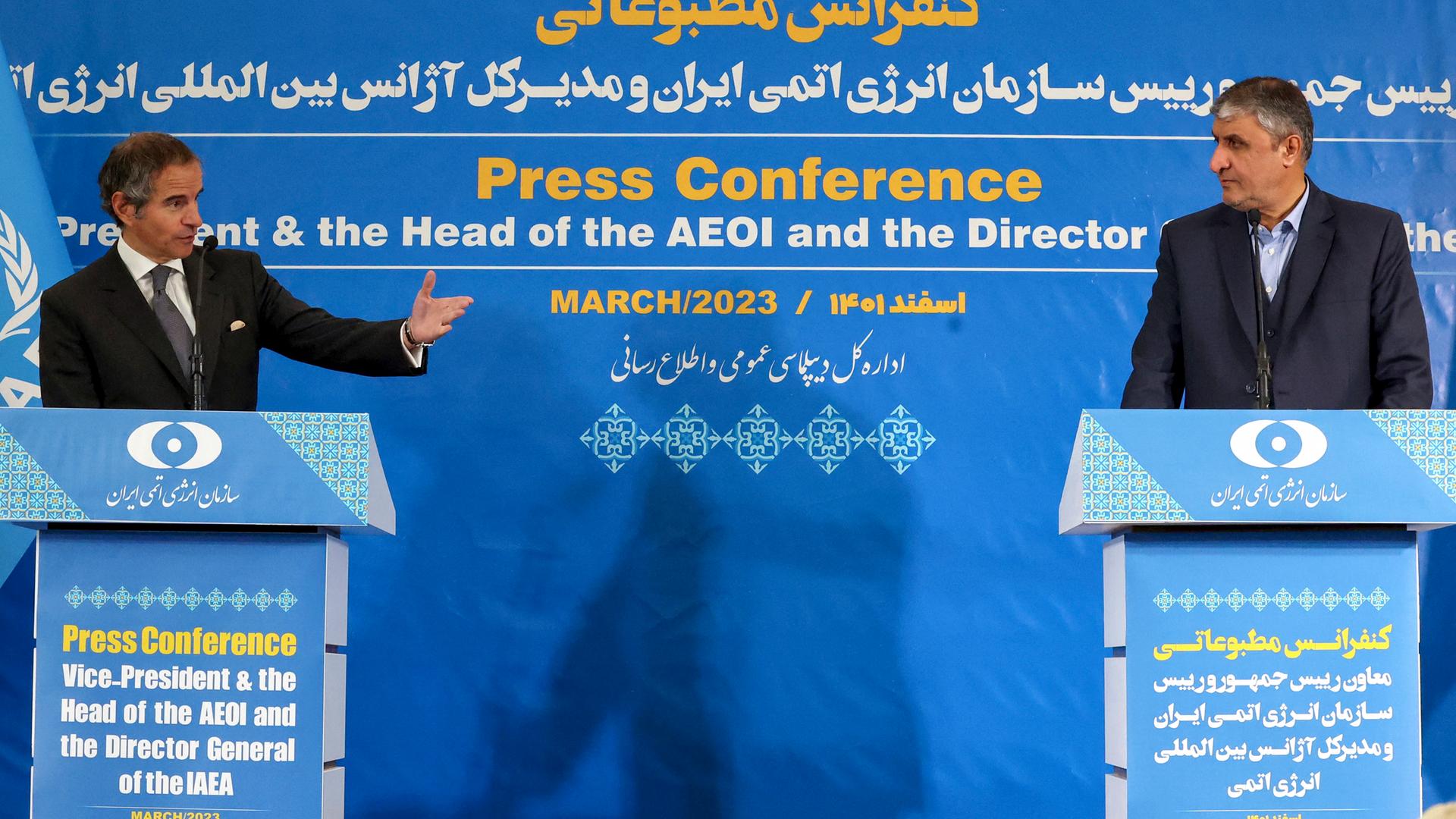 Beide stehen jeweils an einem Rednerpult vor einerblauen Wand mit der Aufschrift "Press Conference"