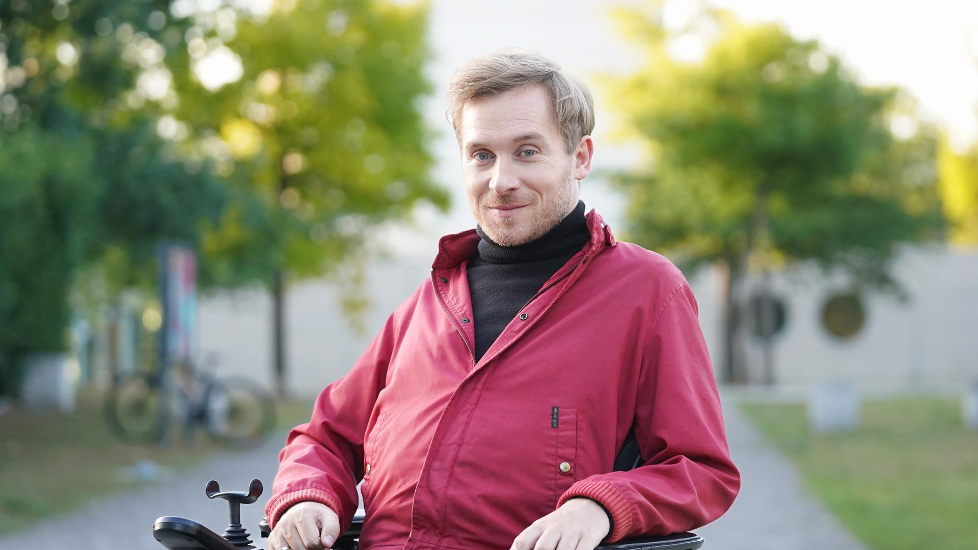 Samuel Koch sitzt in einem Roll-Stuhl. Im Hintergrund sind Bäume.