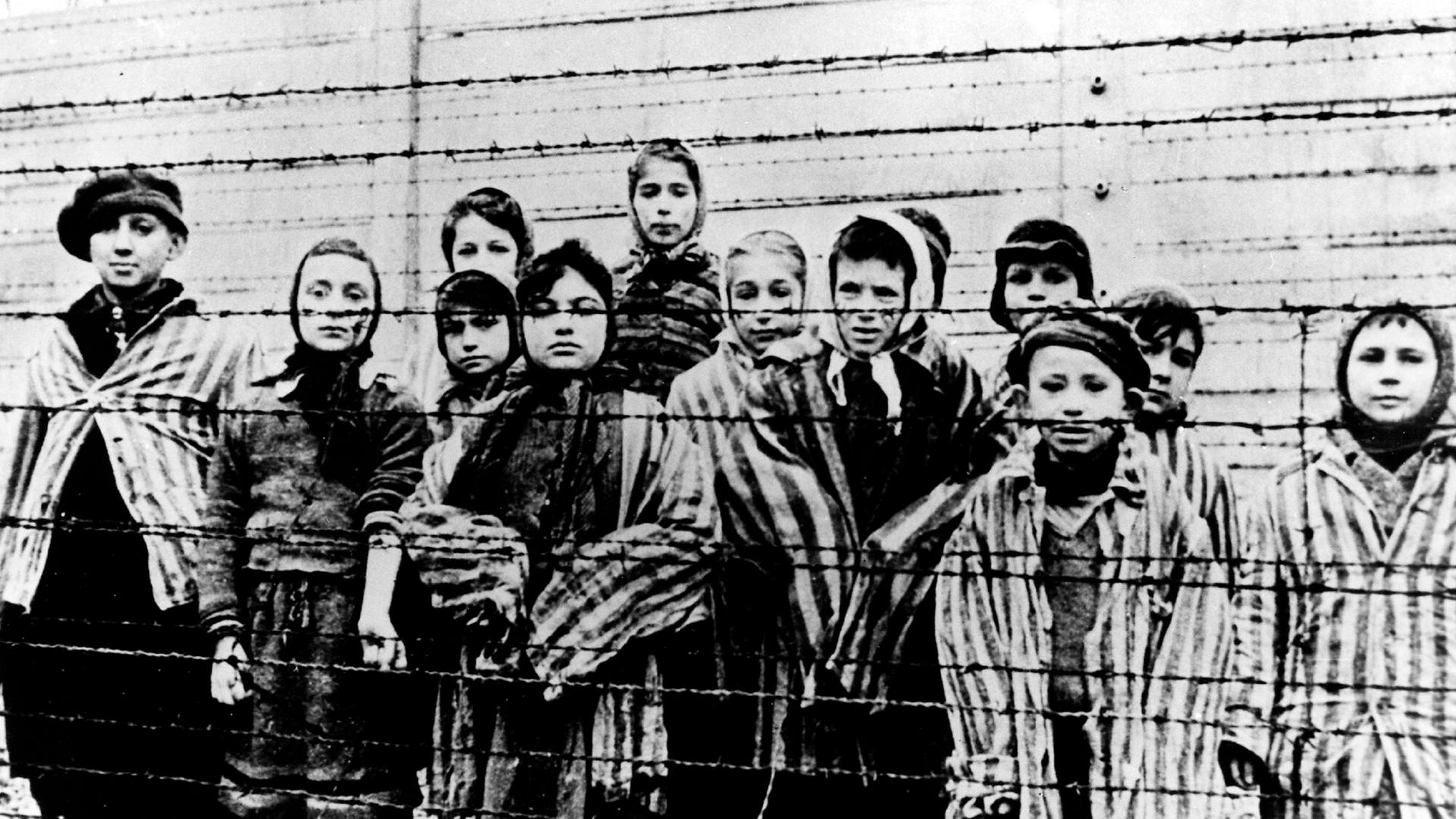 Kinder in Häftlingskleidung hinter einem Stacheldrahtzaun nach der Befreiung des Vernichtungslagers Ausschwitz durch die Rote Armee 1945.