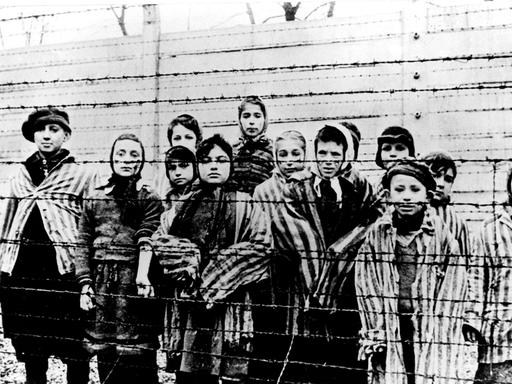 Kinder in Häftlingskleidung hinter einem Stacheldrahtzaun nach der Befreiung des Vernichtungslagers Ausschwitz durch die Rote Armee 1945.