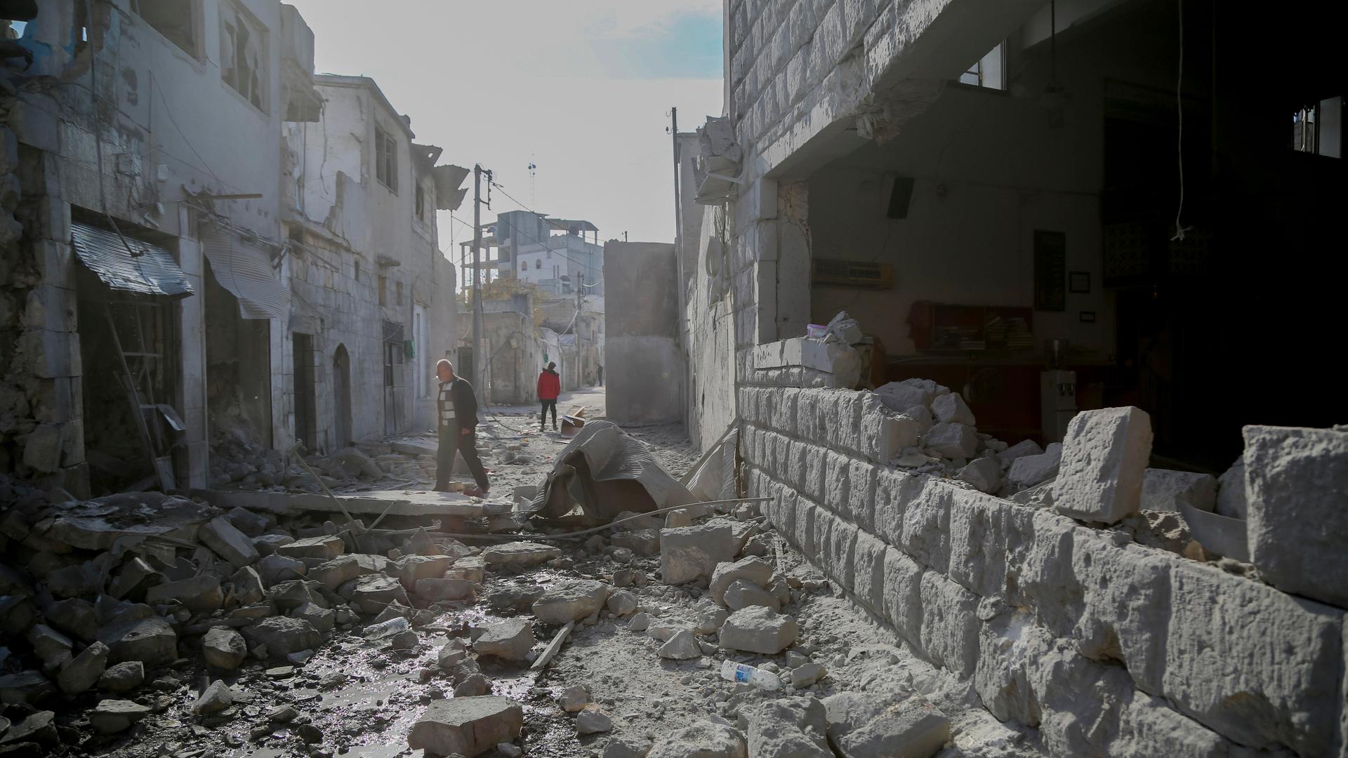 Zwei Personen gehen durch eine Straße in der Nähe von Idlib, auf der große Brocken von den zerstörten Häusern liegen. Zwei Personen gehen durch eine Straße in der Nähe von Idlib, auf der große Brocken von den zerstörten Häusern liegen.